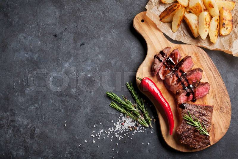 Grilled sliced beef steak on cutting board over stone table. Top view with copy space, stock photo