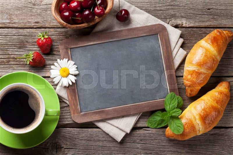Blackboard for your text, croissants, berries, flowers and coffee cup. Top view with copy space, stock photo