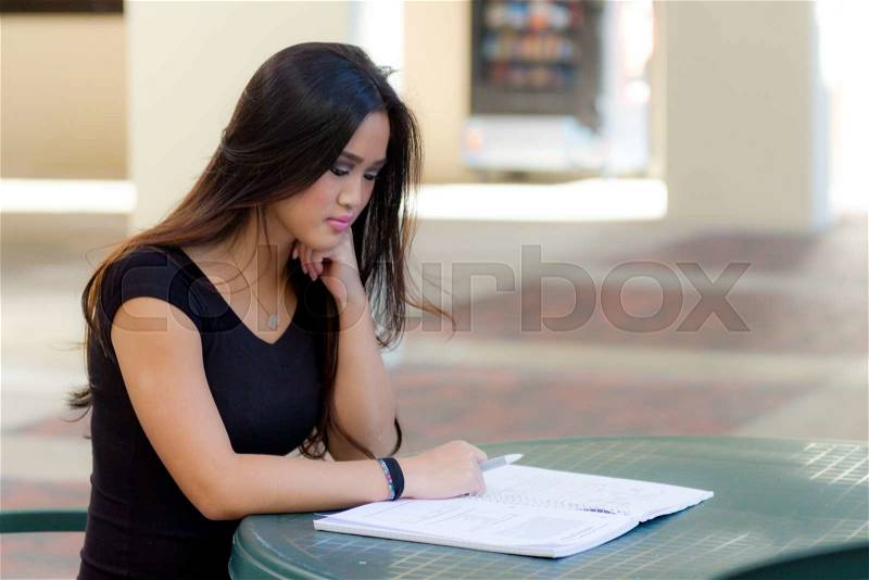 Young asian female student sitting at table reading notebook. Studying for exam, stock photo