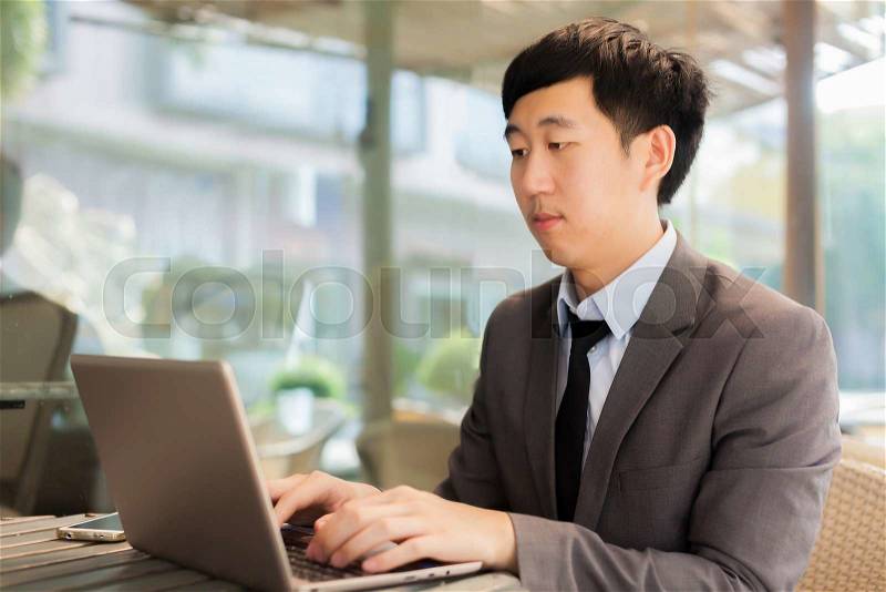 Young Asian businessman working with his laptop in outdoor scene, stock photo