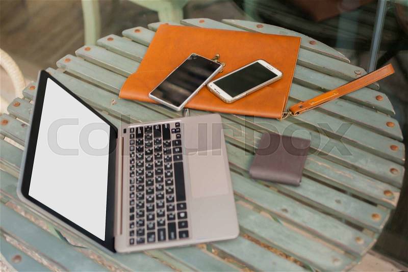 Laptop, smartphones, wallets, and leather bag in outdoor working space, stock photo