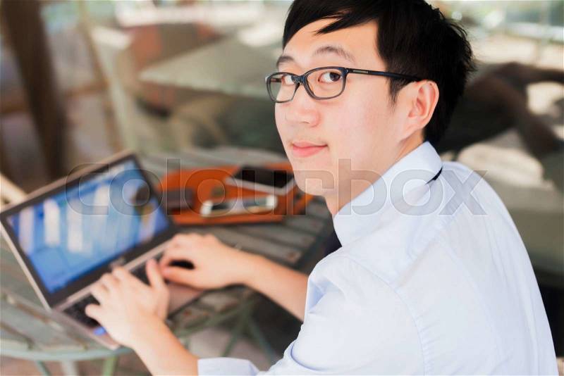 Young Asian businessman working on laptop in outdoor workplace, stock photo