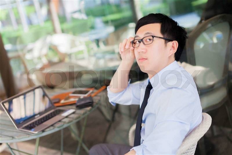 Young Asian businessman working on laptop in outdoor workplace, stock photo