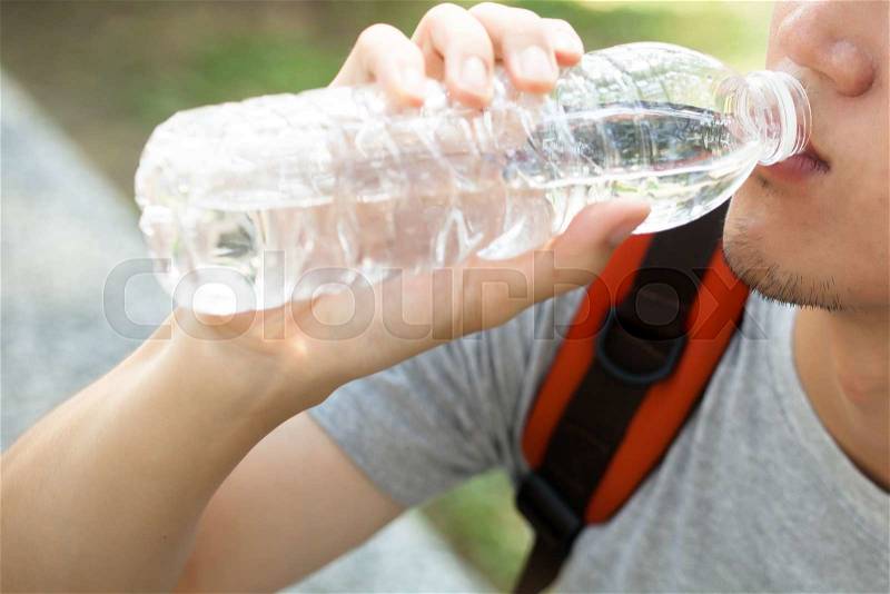 Close up of man drinking mineral water from bottle in the park - health care concept, stock photo
