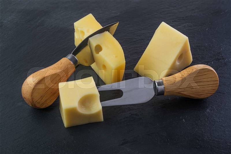 Three pieces of cheese on a black stone slate plate with knife and fork, stock photo