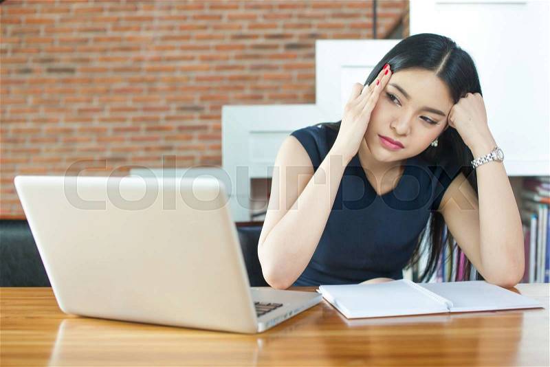 Asian Woman Thinking and Serious in front of Laptop in Modern Office, stock photo