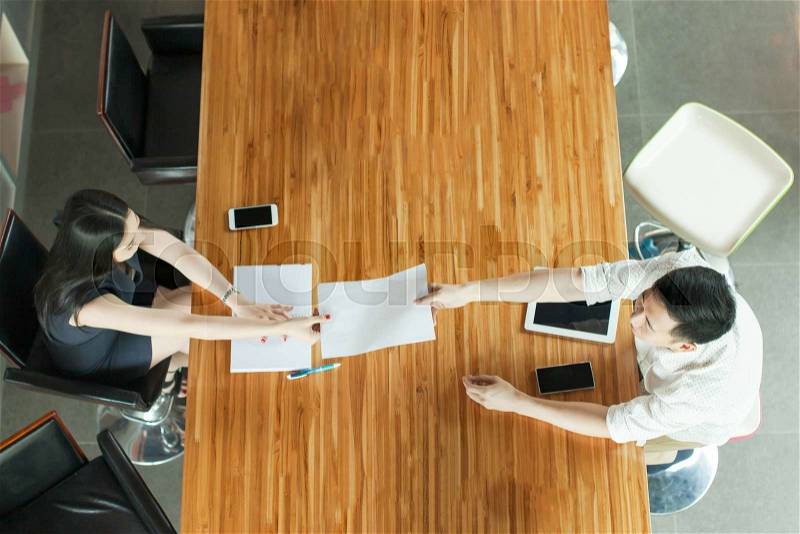Top View of Business People sitting behind meeting desk, handing out documents, stock photo