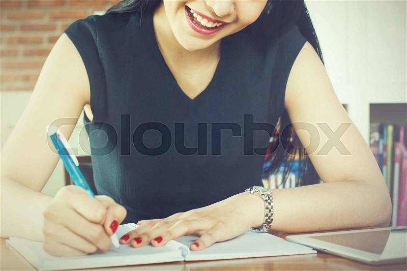 Beautiful woman smiling and writing a notebook on table (Focus on Mouth), stock photo