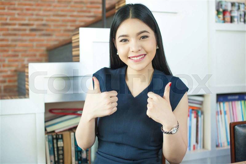 Asian woman giving double thumbs up in modern office, stock photo