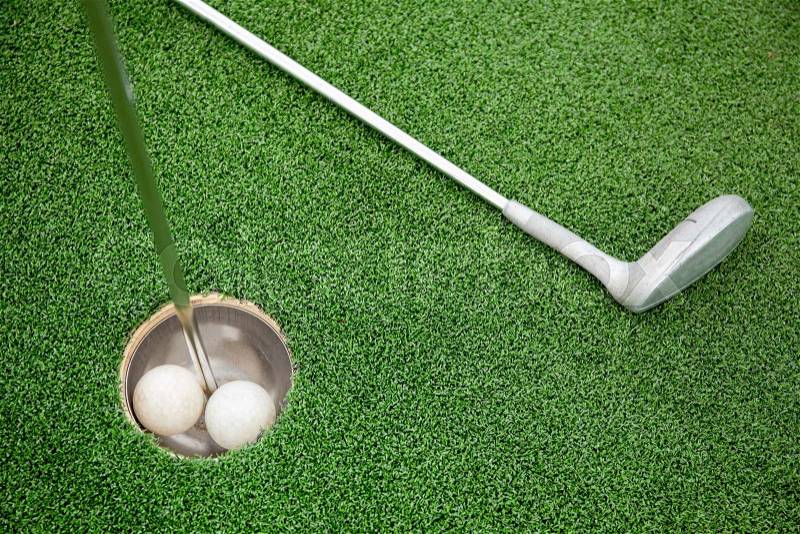 Putting golf club on green grass with golf ball in the hole - top view, stock photo
