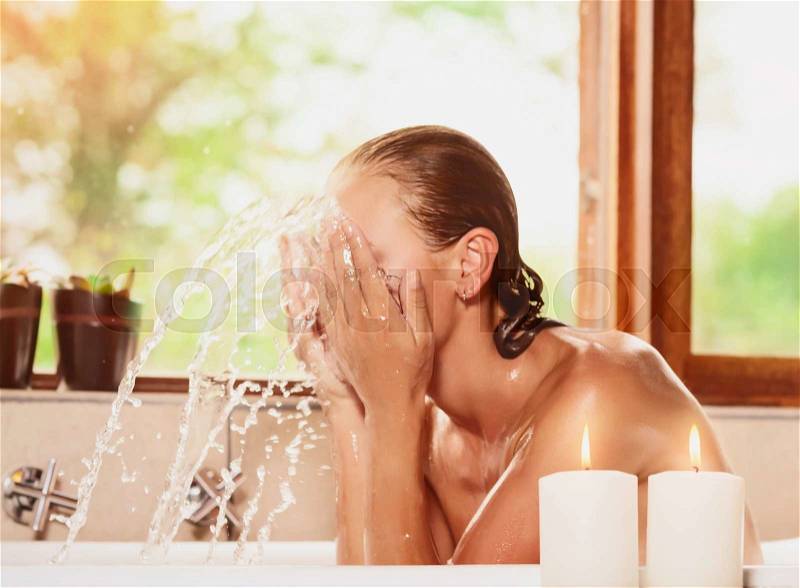 Female washing up face and splashing water in the bathtub, healthy lifestyle, taking bath in a relaxing atmosphere at home, stock photo