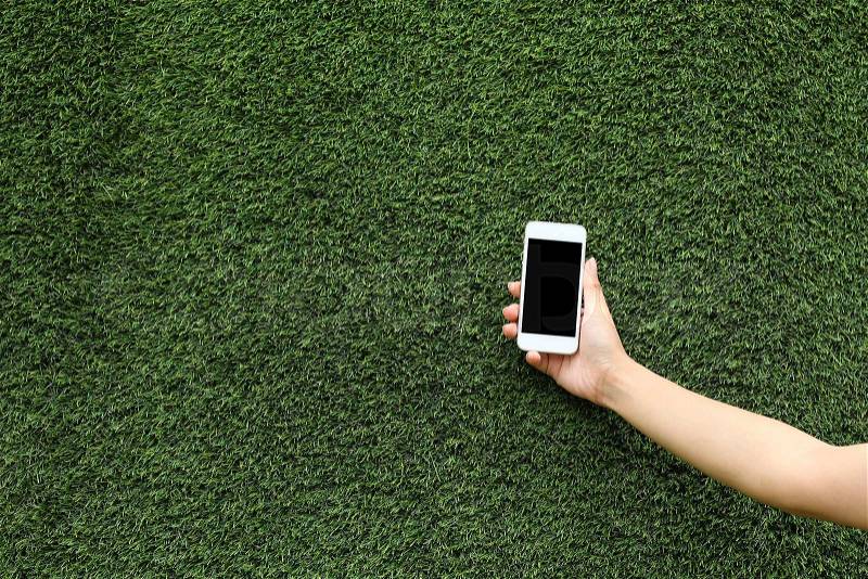 Hand holding mobile phone with green grass background, stock photo