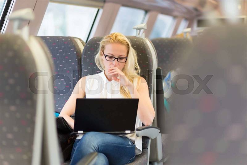 Businesswoman sitting and traveling by train working on laptop, stock photo