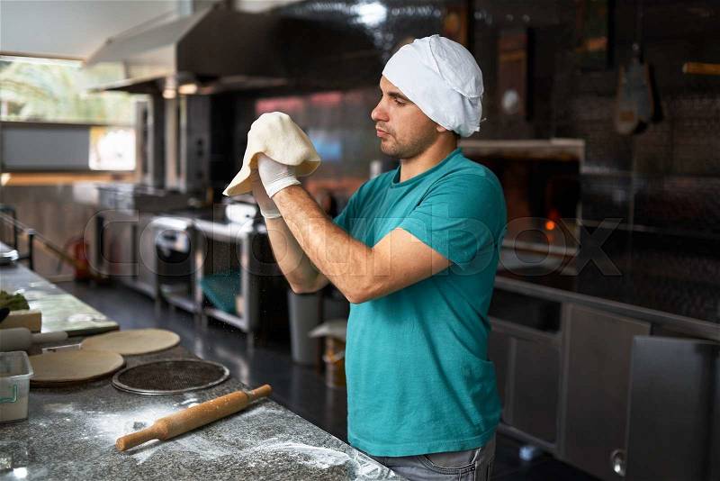 Chef rolls the dough by hand for pizza, side view, stock photo