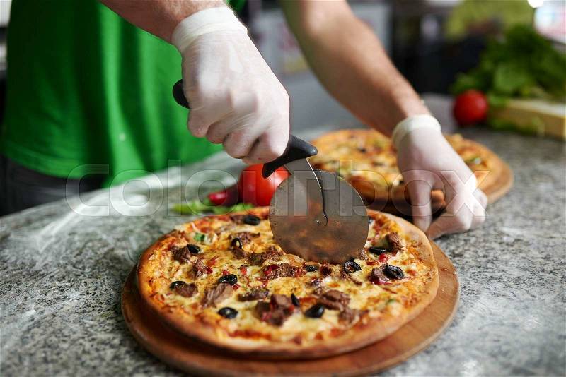 Chef cuts the freshly prepared pizza on a wooden substrate, stock photo