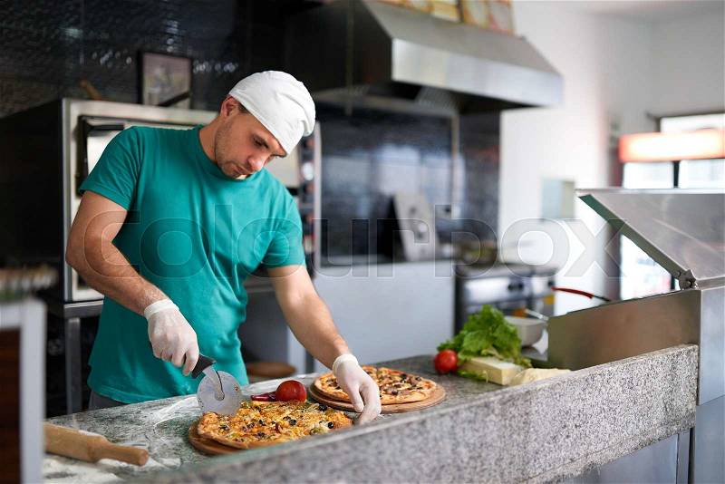 Chef cuts the freshly prepared pizza on a wooden substrate, stock photo