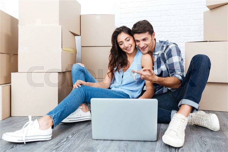 Smiling couple ready to move out looking for a new apartment on their laptop, stock photo