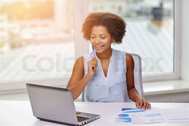 Education, business, statistics and technology concept - happy african american businesswoman or student with laptop computer and papers at office, stock photo