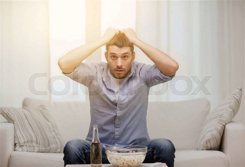 Sports, happiness and people concept - sad man watching sports on tv and supporting team at home, stock photo