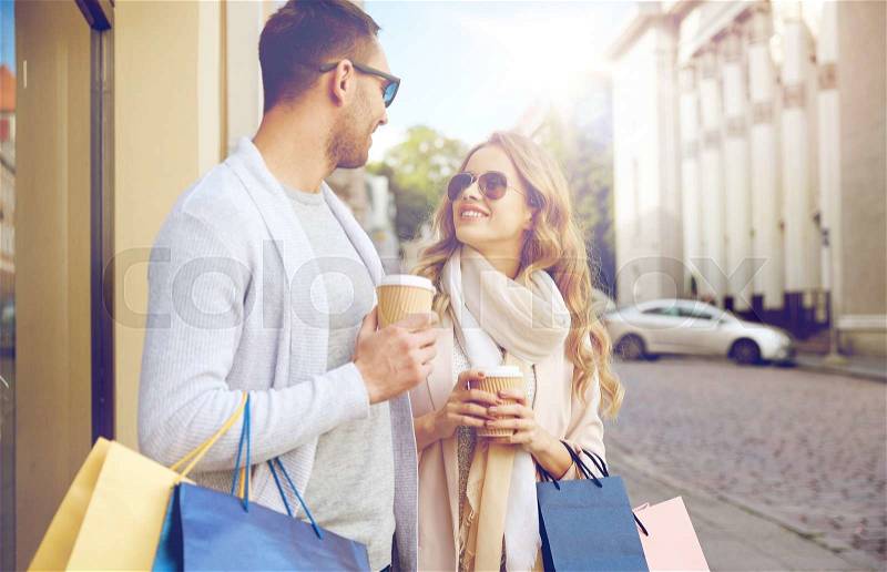 Sale, consumerism and people concept - happy couple with shopping bags and coffee paper cups at shop window in city, stock photo