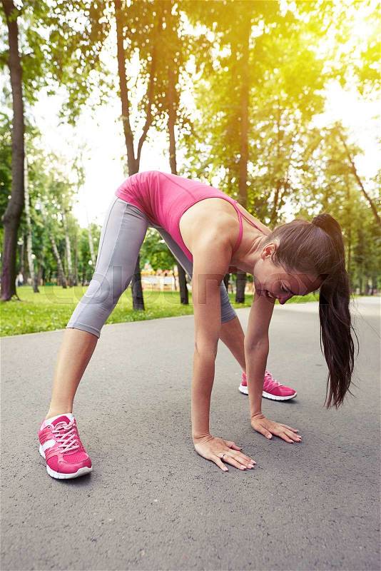 Young sporty sexy lady is stretching legs while doing workout exercises in the park, stock photo