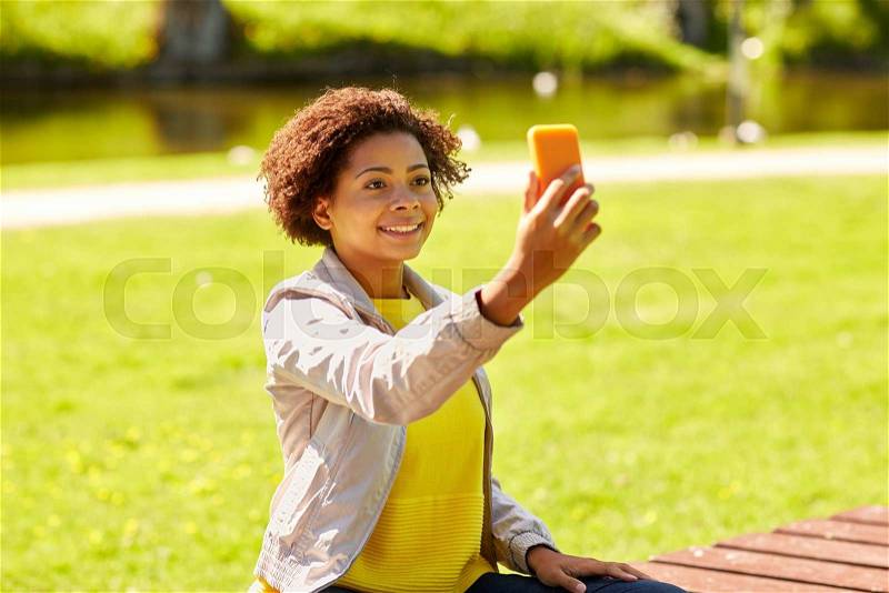 Technology, communication and people concept - happy african woman taking selfie with smartphone at summer park, stock photo