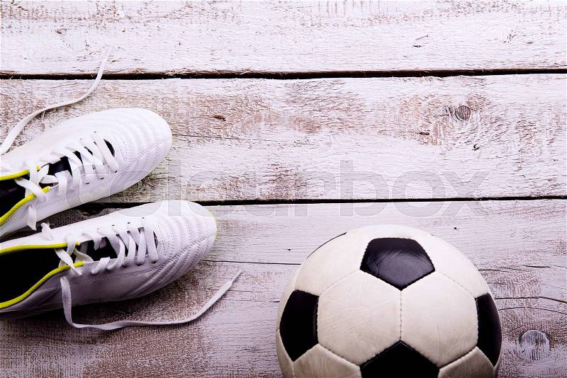 Soccer ball, cleats against wooden floor, studio shot on white background. Flat lay, copy space, stock photo