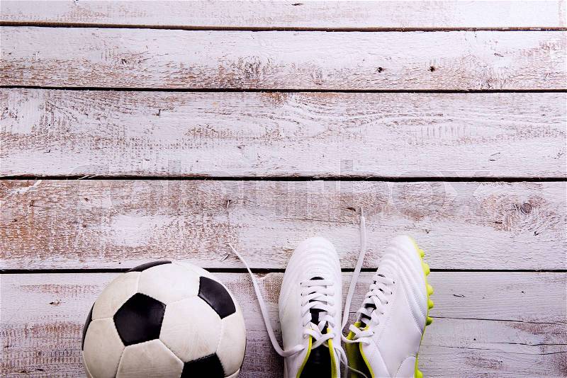 Soccer ball, cleats against wooden floor, studio shot on white background. Flat lay, copy space, stock photo