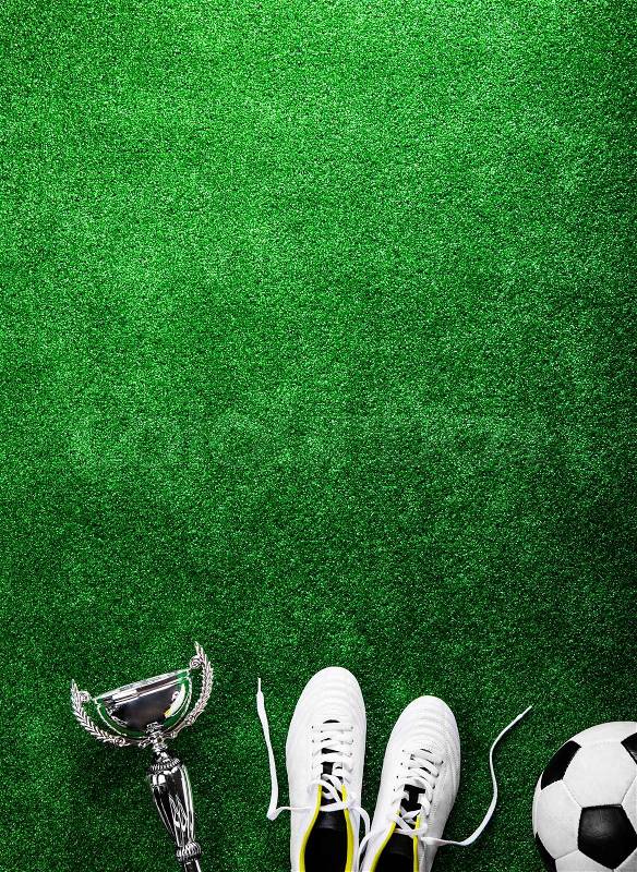 Soccer ball, cleats and trophy against artificial turf, studio shot on green background. Copy space, stock photo