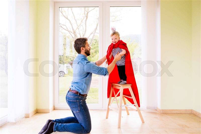 Hipster father with his cute little princess daughter jumping into his arms, wearing red cape, stock photo