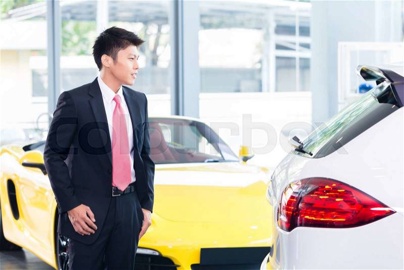 Chinese man buying luxury car in dealership, stock photo