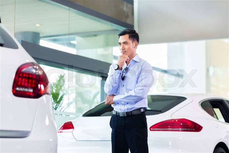 Asian man buying luxury car in dealership, stock photo