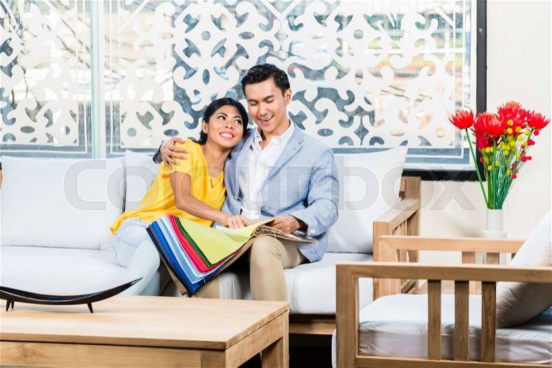 Asian couple buying sofa in furniture store, sitting on couch choosing color and material , stock photo