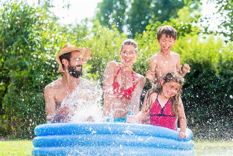 Family in garden pool splashing water cooling down, mother, father and kids having fun together, stock photo