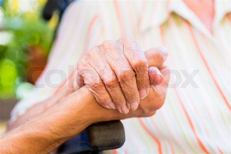 Nurse holding hand of senior woman in wheel chair, stock photo