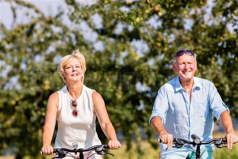 Senior woman and man at bicycle tour on path along field in summer, stock photo