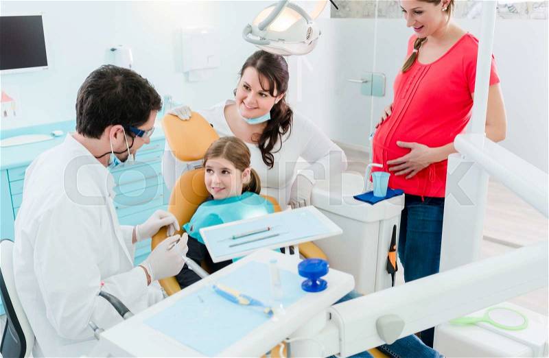 Dentist treating the whole family in his office, pregnant mother and child, stock photo