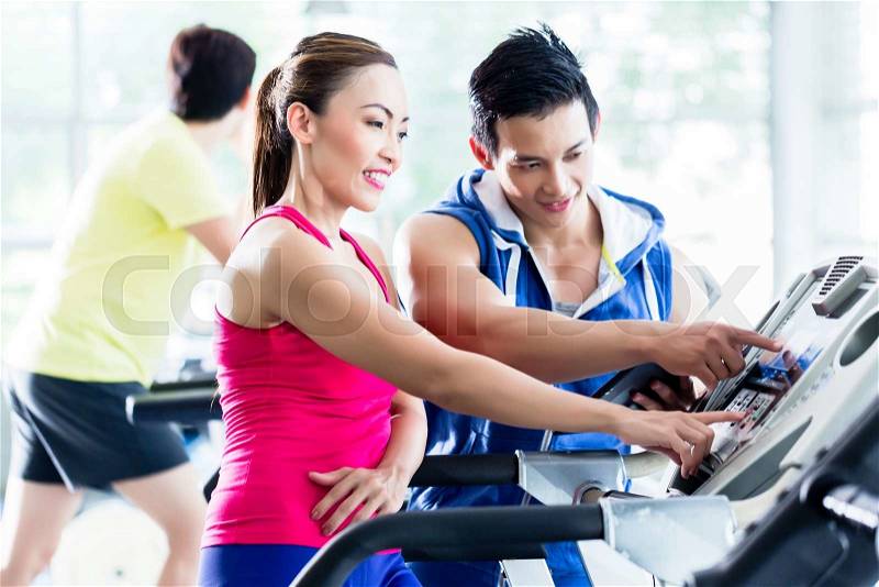 Male instructor evaluating fitness performance of young woman on treadmill in gym, stock photo