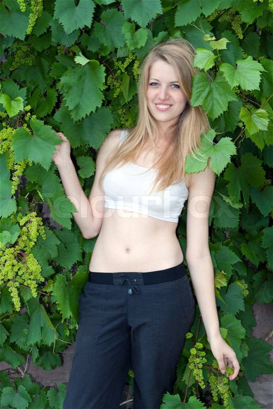 Portrait of the beautiful young blonde with grapes on a green background of foliage, stock photo