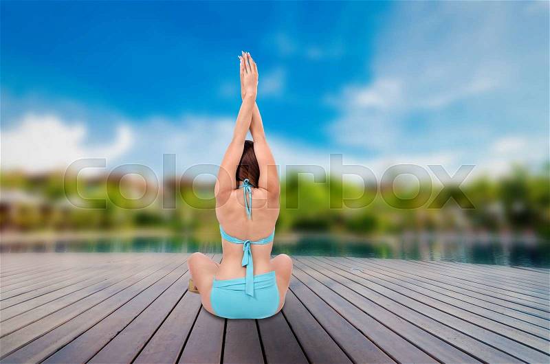 Yoga meditation near pool. Bikini body woman meditating relaxing sitting on wooden terrace tropical summer travel. Health and fitness retreat concept, stock photo