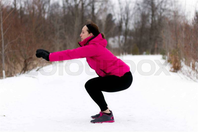 Fit woman doing squats exercises on outdoor winter nature trail. Wellness workout and healthy lifestyle concept, stock photo