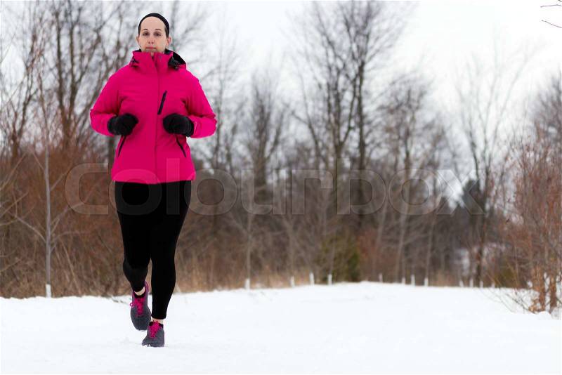 Winter snow runner woman running outside on cold winter day. Fit healthy lifestyle concept with beautiful young fitness model. Caucasian female model jogging outside in full length, stock photo