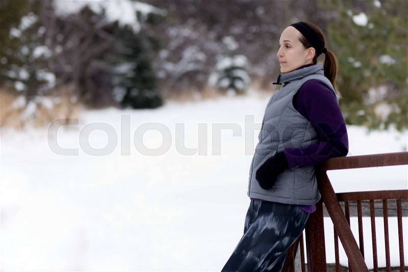 Sporty fit woman in winter running clothing relaxes along nature trail, stock photo