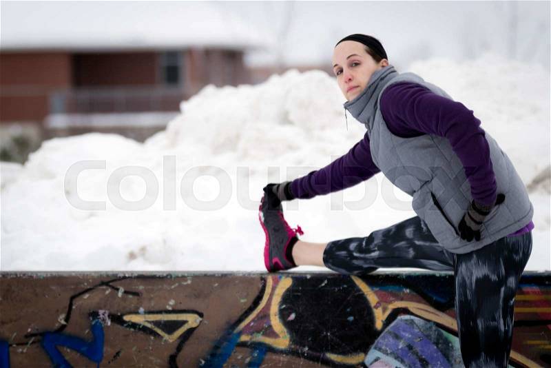 Fit sporty woman outdoors in winter running gear at urban park with graffiti stretching. Fit healthy lifestyle concept, stock photo