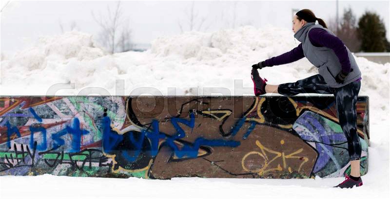 Fit sporty woman outdoors in winter running gear at urban park with graffiti stretching. Fit healthy lifestyle concept, stock photo