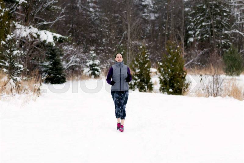 Winter snow runner woman running outside on cold winter day. Fit healthy lifestyle concept with beautiful young fitness model.Caucasian female model jogging outside in full length, stock photo