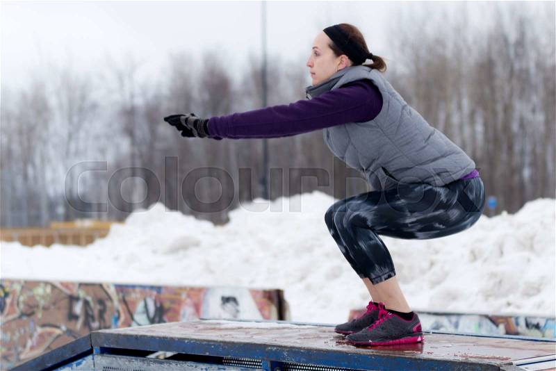 Fit sporty woman outdoors in winter running gear at urban park doing squat exercises. Fit healthy lifestyle concept, stock photo