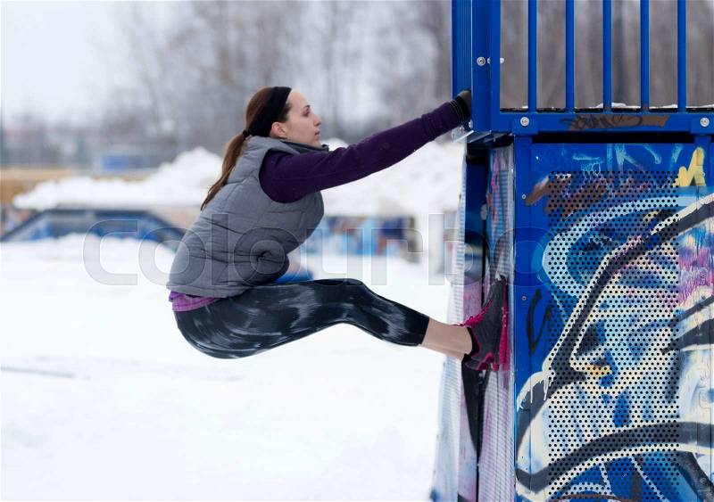 Fit sporty woman outdoors in winter running gear at urban park doing climbing exercises. Fit healthy lifestyle concept, stock photo