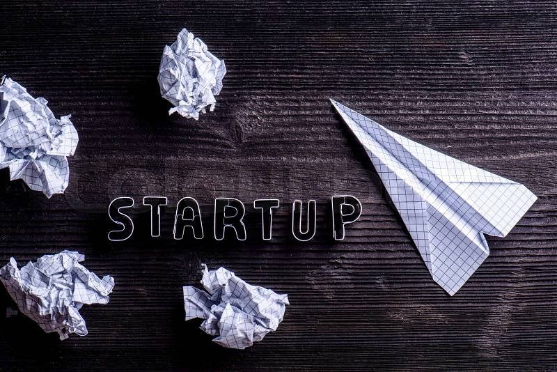 Office desk with start up sign made of cookie cutters, paper airplanes and crumpled paper balls. Flat lay. Workplace. Studio shot on wooden background, stock photo