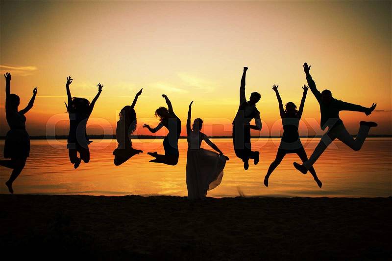 Silhouettes of group of people in a jump at sunset. Eight young men and women depicted in a jump against the evening sky and the river. Feeling of ease and flight. Colors of a decline, stock photo